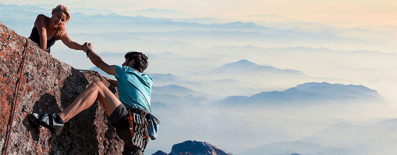 Eine Bergsteigerin reicht einem anderen Bergsteiger die Hand und hilft ihm